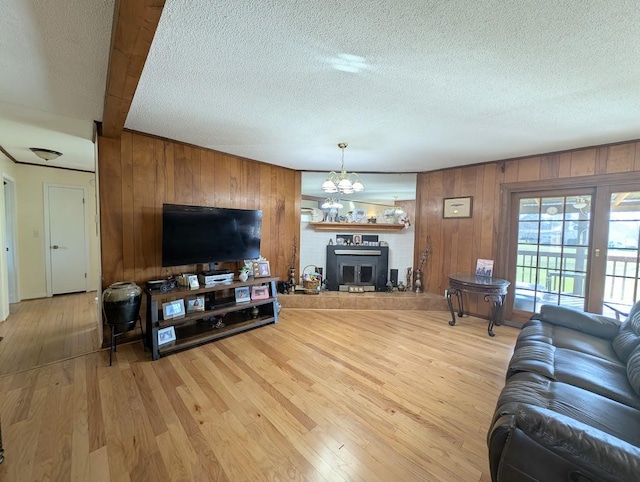 living room with light wood-type flooring, a chandelier, a textured ceiling, and wooden walls