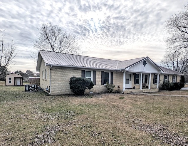 view of front of home with an outdoor structure, a front lawn, a storage unit, brick siding, and metal roof