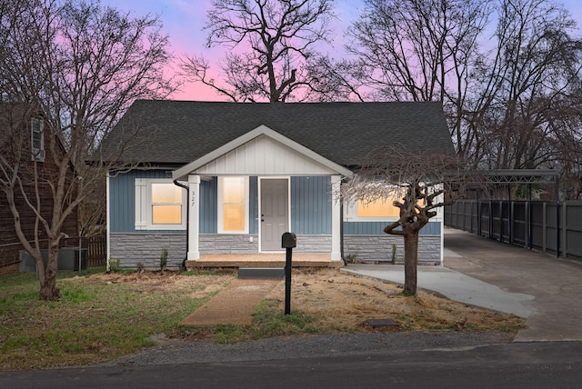 view of front of house with stone siding, a shingled roof, fence, and a porch