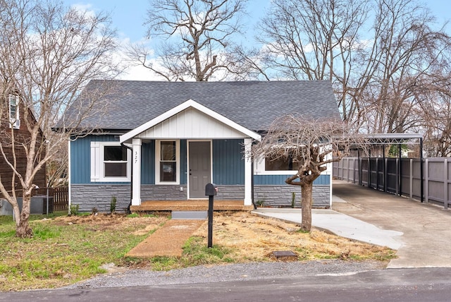 view of front of property with stone siding, a shingled roof, concrete driveway, and fence