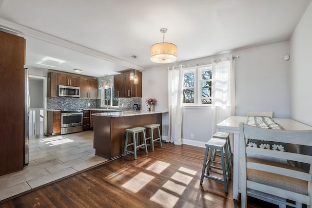 kitchen featuring backsplash, dark wood-type flooring, stainless steel appliances, kitchen peninsula, and a breakfast bar area