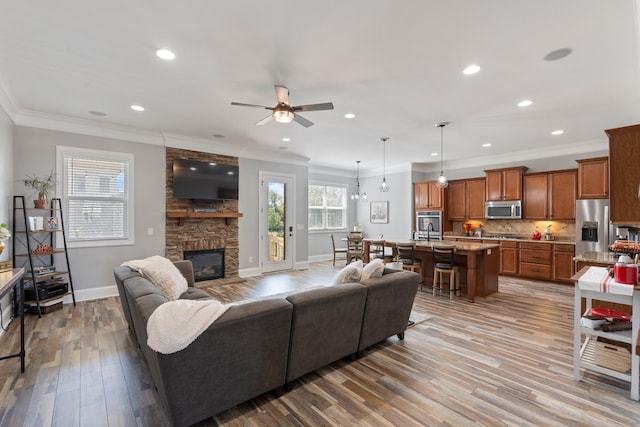 living room with a fireplace, ornamental molding, ceiling fan, and light hardwood / wood-style floors