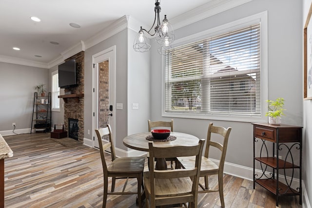 dining area with hardwood / wood-style flooring, crown molding, an inviting chandelier, and a stone fireplace