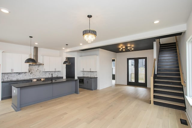 kitchen with decorative light fixtures, white cabinetry, gray cabinetry, wall chimney range hood, and a center island with sink