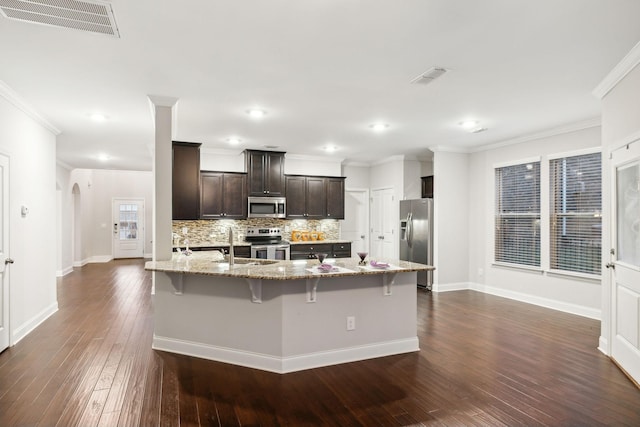 kitchen featuring a center island with sink, stainless steel appliances, a breakfast bar, light stone countertops, and dark brown cabinets