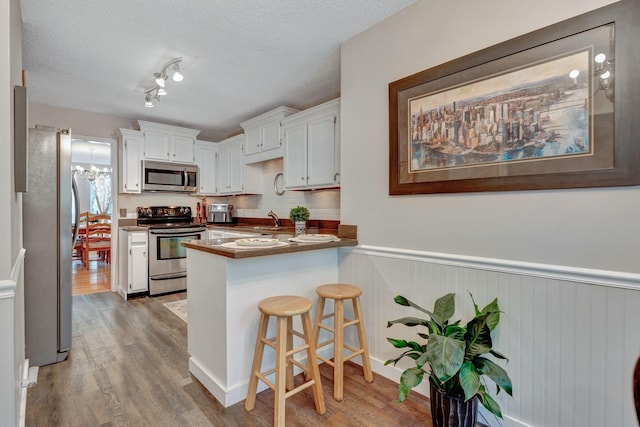 kitchen featuring sink, white cabinetry, appliances with stainless steel finishes, a kitchen breakfast bar, and kitchen peninsula