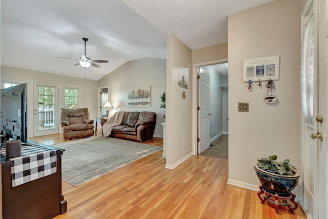 living room featuring ceiling fan, vaulted ceiling, light hardwood / wood-style flooring, and a textured ceiling