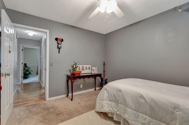 bedroom with ceiling fan, light colored carpet, and a textured ceiling