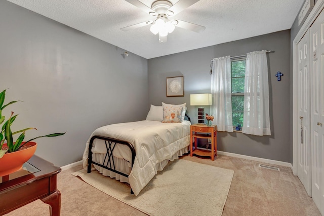 bedroom with ceiling fan, light carpet, a closet, and a textured ceiling