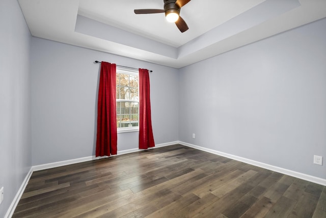 empty room with a tray ceiling, ceiling fan, and dark wood-type flooring