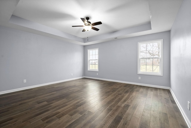 empty room with a raised ceiling, ceiling fan, and dark hardwood / wood-style floors