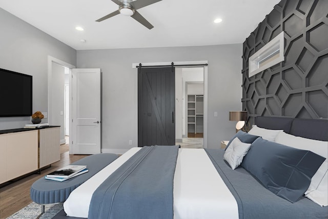 bedroom featuring a closet, a spacious closet, ceiling fan, hardwood / wood-style floors, and a barn door