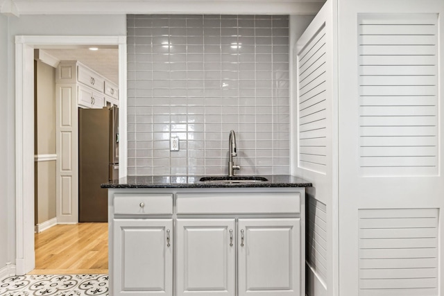 kitchen with tasteful backsplash, white cabinets, stainless steel refrigerator, sink, and dark stone countertops