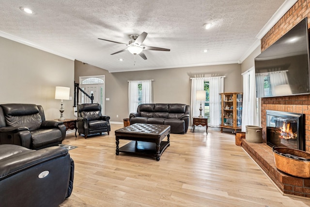 living room featuring a textured ceiling, ceiling fan, light hardwood / wood-style floors, a fireplace, and ornamental molding