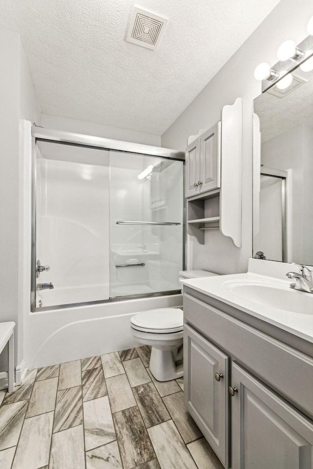 full bathroom with enclosed tub / shower combo, vanity, toilet, and a textured ceiling