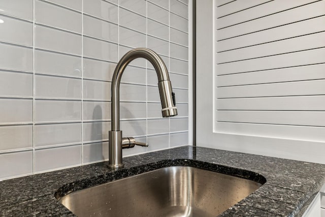 room details with dark stone countertops, white cabinetry, sink, and backsplash