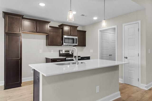 kitchen with appliances with stainless steel finishes, light hardwood / wood-style flooring, a center island with sink, decorative light fixtures, and sink