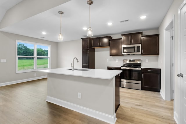 kitchen with stainless steel appliances, light hardwood / wood-style floors, pendant lighting, sink, and a kitchen island with sink