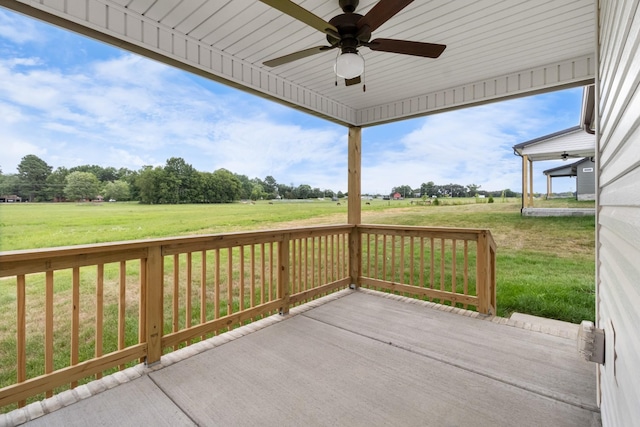 wooden terrace with a rural view, a lawn, and ceiling fan