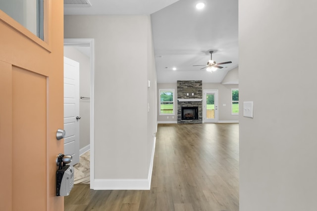 unfurnished living room featuring ceiling fan, a stone fireplace, vaulted ceiling, and hardwood / wood-style floors