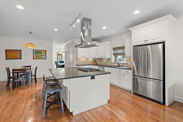 kitchen featuring appliances with stainless steel finishes, tasteful backsplash, island range hood, a center island, and white cabinetry