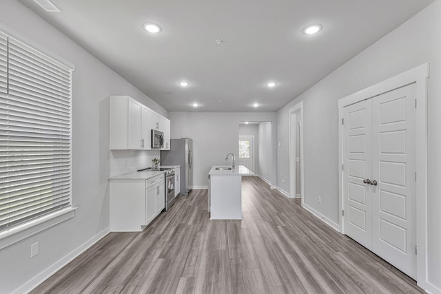 kitchen with appliances with stainless steel finishes, sink, light wood-type flooring, white cabinetry, and a kitchen island with sink