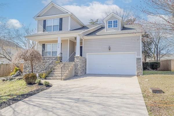 view of front facade with a porch, driveway, a garage, and fence