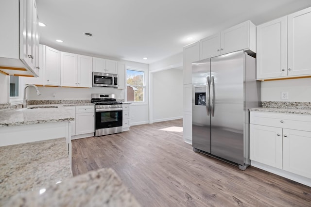 kitchen featuring light wood-type flooring, sink, light stone counters, appliances with stainless steel finishes, and white cabinets