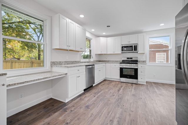 kitchen featuring white cabinets, appliances with stainless steel finishes, light stone counters, and hardwood / wood-style floors