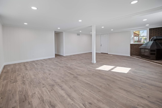 basement with a wood stove and light hardwood / wood-style flooring