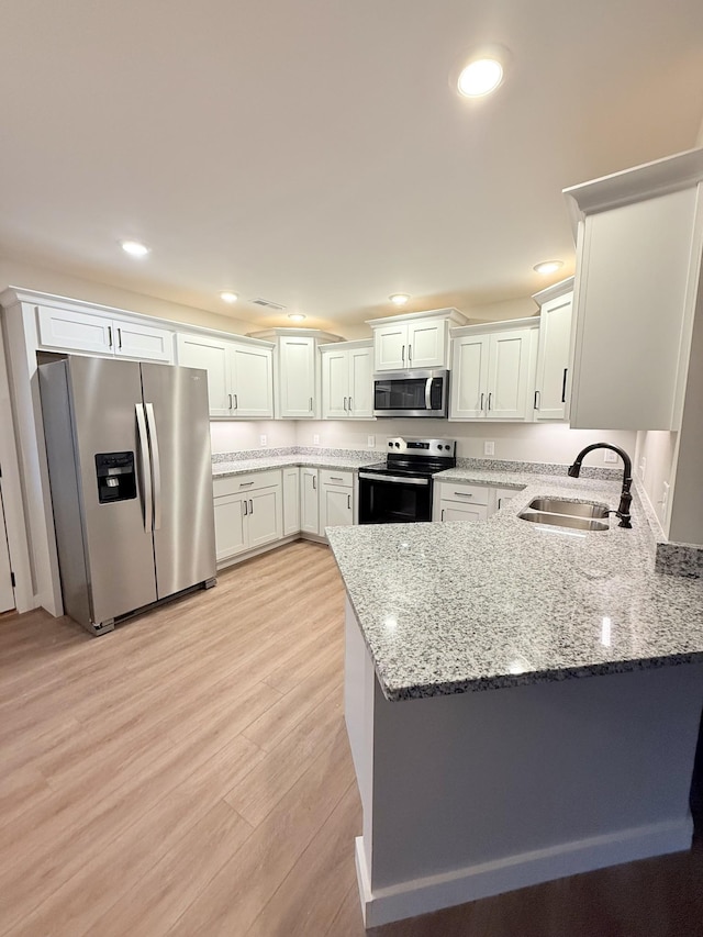 kitchen featuring appliances with stainless steel finishes, light stone counters, white cabinets, light hardwood / wood-style floors, and sink