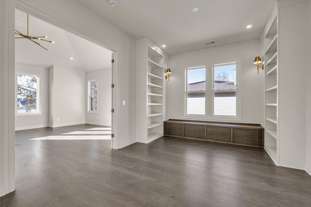 empty room featuring built in features, a chandelier, dark hardwood / wood-style flooring, and plenty of natural light