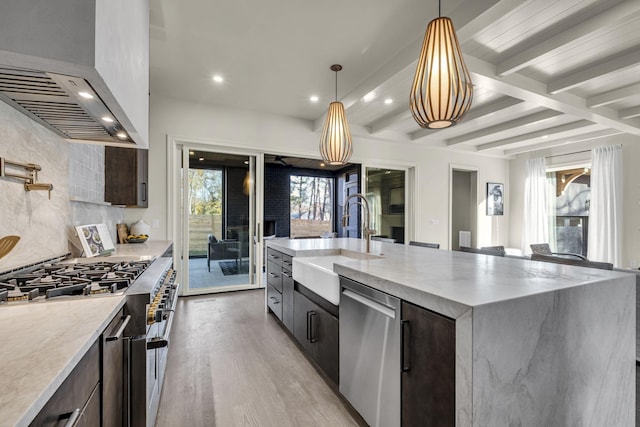 kitchen with appliances with stainless steel finishes, extractor fan, sink, light hardwood / wood-style floors, and a spacious island