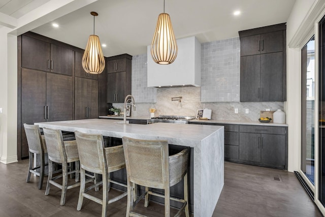 kitchen with sink, a kitchen island with sink, wall chimney exhaust hood, and decorative backsplash