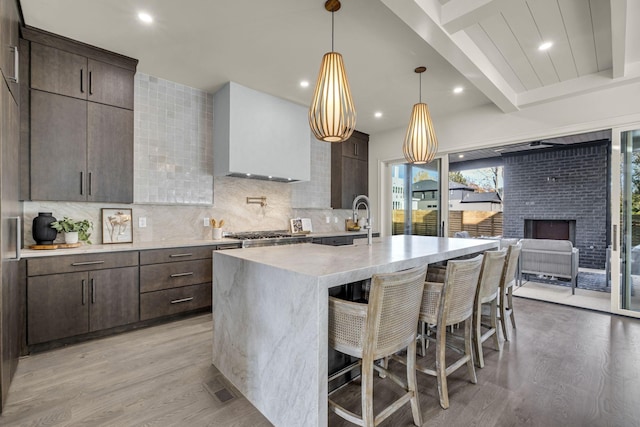 kitchen featuring a center island with sink, a kitchen bar, light hardwood / wood-style floors, beam ceiling, and decorative backsplash