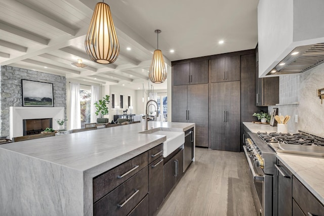 kitchen featuring appliances with stainless steel finishes, wall chimney range hood, pendant lighting, sink, and a large island with sink