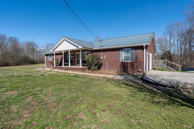 back of house with a porch, metal roof, brick siding, and a lawn