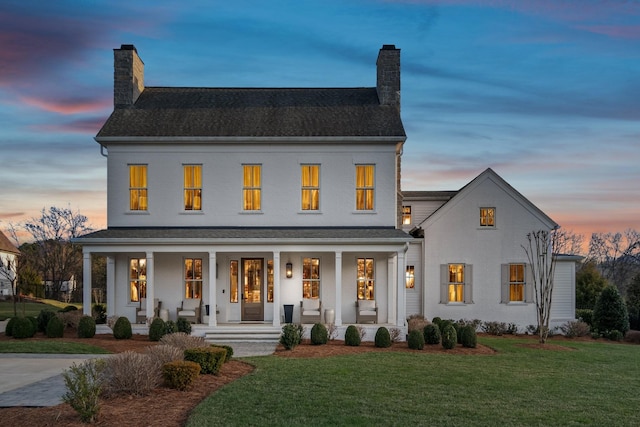 view of front facade featuring a chimney, a porch, and a yard