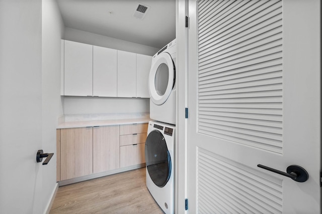 washroom featuring light hardwood / wood-style floors, cabinets, and stacked washer / drying machine