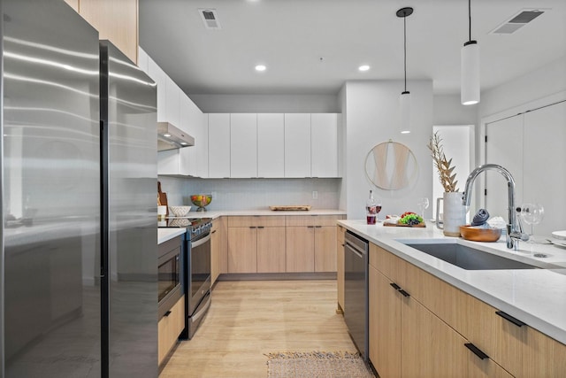 kitchen featuring sink, pendant lighting, stainless steel appliances, light brown cabinetry, and white cabinets