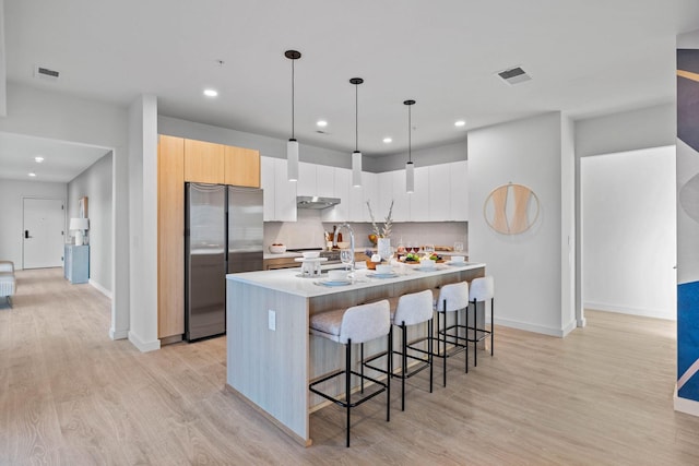 kitchen with hanging light fixtures, white cabinets, a breakfast bar, stainless steel fridge, and a kitchen island with sink