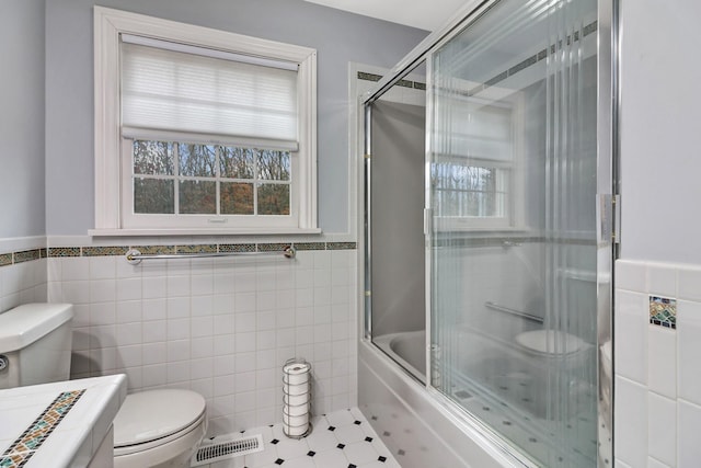 full bathroom featuring tile patterned flooring, toilet, tile walls, vanity, and bath / shower combo with glass door