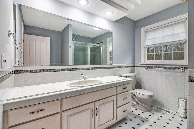 bathroom featuring tile patterned flooring, toilet, walk in shower, tile walls, and vanity