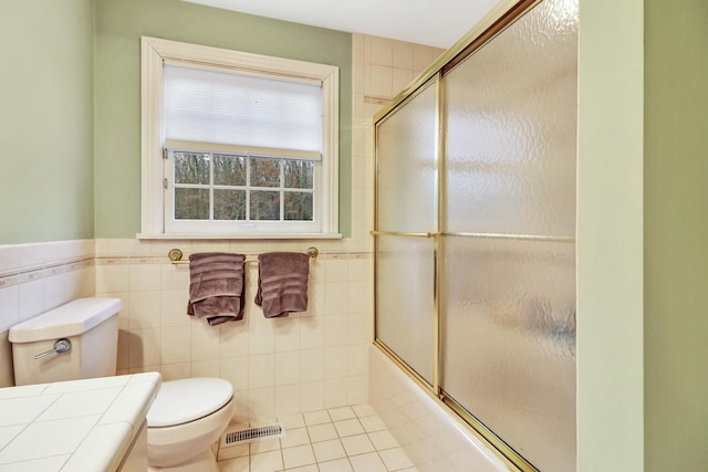 bathroom with toilet, tile walls, tile patterned flooring, and enclosed tub / shower combo