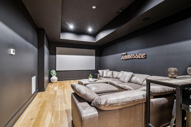 cinema room featuring a tray ceiling and light wood-type flooring