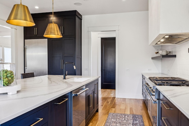 kitchen with sink, light stone counters, light hardwood / wood-style floors, stainless steel appliances, and hanging light fixtures