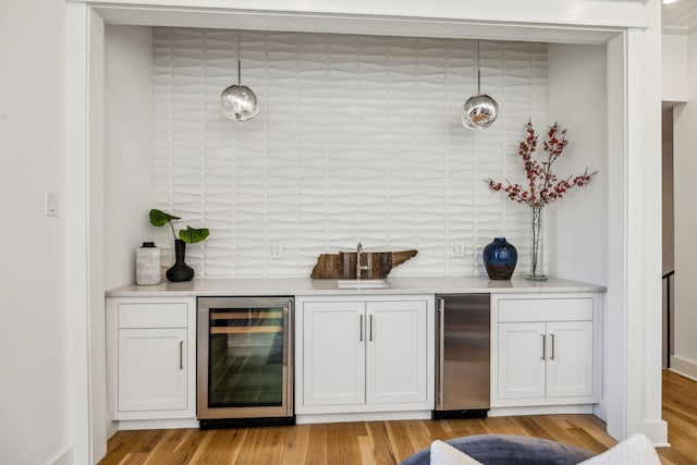 bar featuring hanging light fixtures, white cabinets, light wood-type flooring, fridge, and wine cooler