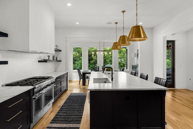 kitchen featuring a center island with sink, sink, double oven range, decorative light fixtures, and light hardwood / wood-style floors