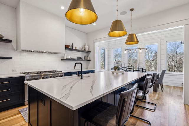 kitchen with hanging light fixtures, a breakfast bar, sink, stainless steel range, and light stone counters