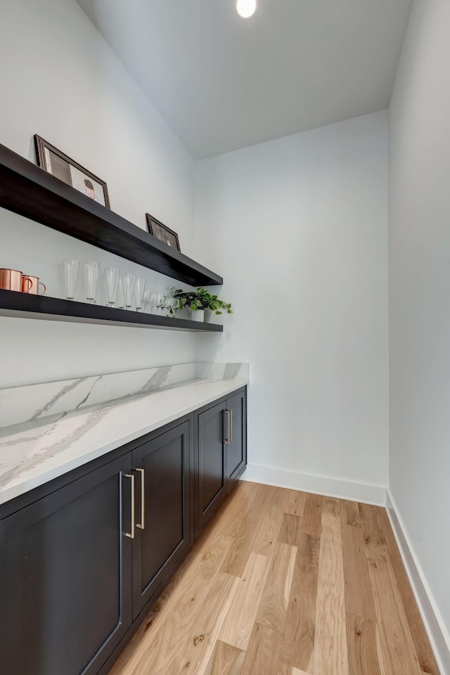 bar with light stone countertops and light hardwood / wood-style flooring